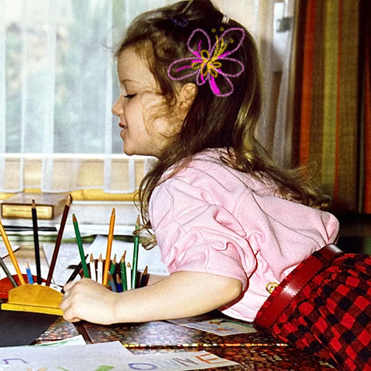 Muriel Thoma Kinderfoto Mädchen an Tisch mit Farbstiften und gezeichneter Blume im Haar